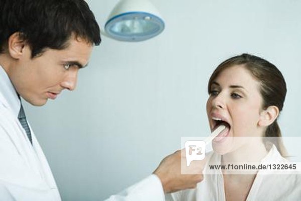 Arzt hält die Zunge der Frau mit Zungenspatel fest