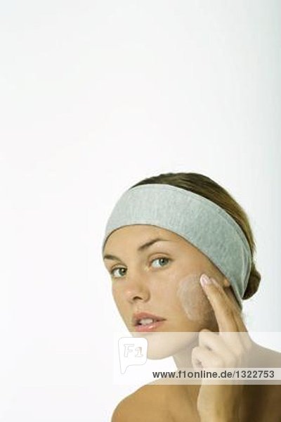 Young woman applying facial cleanser to cheek  head and shoulders