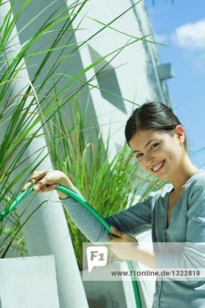 Junge Frau gießt Pflanzen mit Gartenschlauch