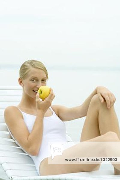 Teenagermädchen im Badeanzug  im Sessel sitzend  Apfel essend