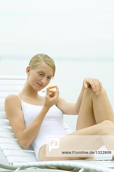 Teenagermädchen im Badeanzug  im Loungesessel sitzend  mit Karottenstäbchen in der Hand
