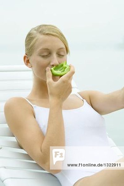 Teenagermädchen im Badeanzug  im Sessel sitzend  riechendes Stück grüner Pfeffer