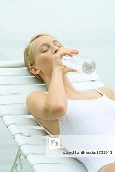 Teenagermädchen im Badeanzug  im Sessel sitzend  aus der Wasserflasche trinkend  Augen geschlossen