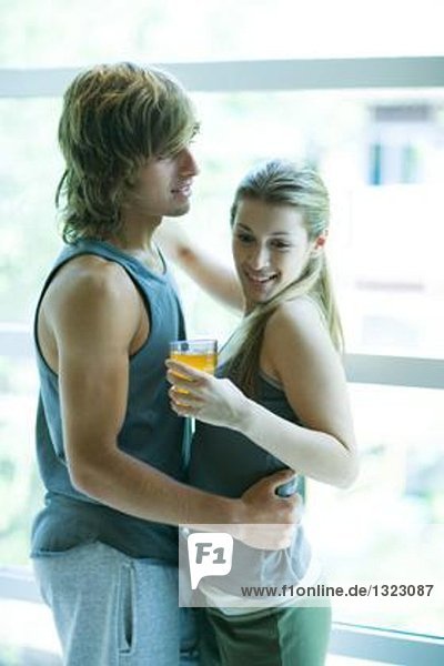 Junges Paar in Trainingsbekleidung  Frau hält Drink  Mann hält Frau um die Taille