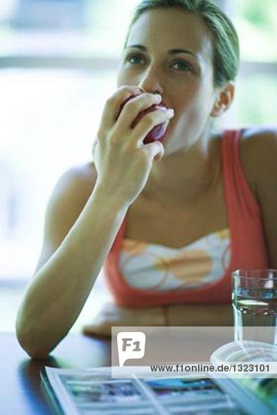 Junge Frau sitzend mit Magazin und Glas Wasser  Apfel essend