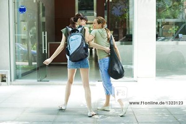 Zwei junge Frauen in Straßenkleidung gehen auf den Eingang zum Fitnessstudio zu.
