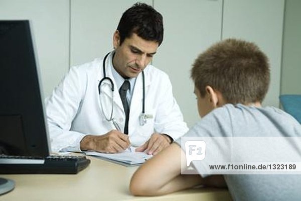 Der Arzt sitzt gegenüber dem Kind und macht sich Notizen.