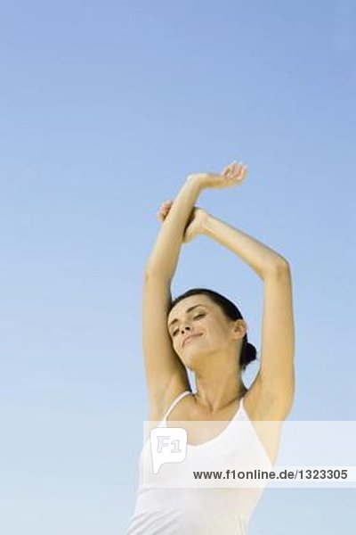 Woman stretching arms overhead  sky in background  low angle view