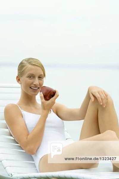 Teenagermädchen im Badeanzug sitzend auf Sessel  Apfel haltend