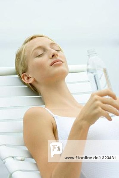 Teenagermädchen im Badeanzug sitzend auf einem Sessel  hält eine Flasche Wasser in der Hand.