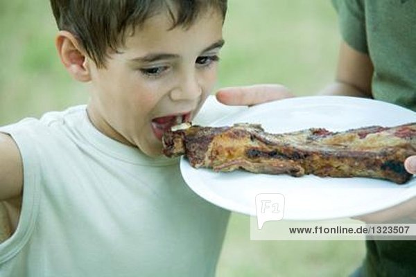 Junge isst gegrilltes Fleisch vom Teller