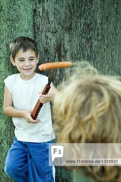 Junge hält Hot Dog am Ende der großen Gabel  zeigt Freund