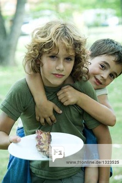 Junge hält gegrilltes Fleisch auf dem Teller  Freund reitet Huckepack