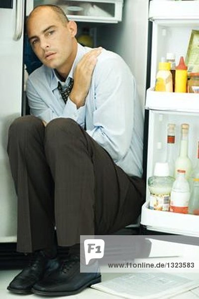 Mann im offenen Kühlschrank sitzend  Arme kreuzend