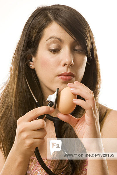 Junge Frau hält Stethoskop auf Ei