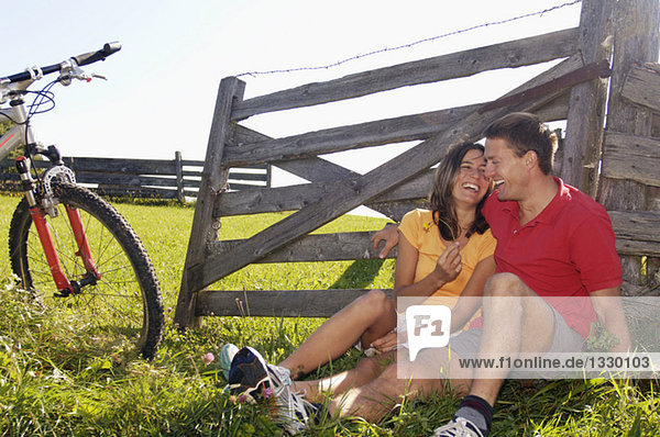 Couple sitting in meadow  leaning on wooden railing