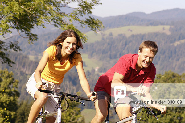 Junges Paar beim Radfahren  lächelnd  Berge im Hintergrund