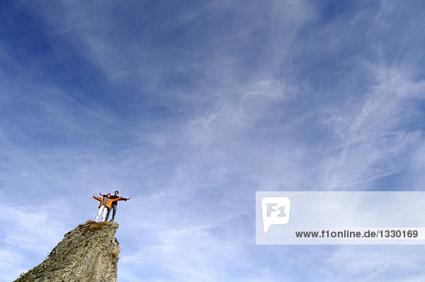 Junges Paar auf Berggipfel stehend,  Arme ausgestreckt,  Tiefblick