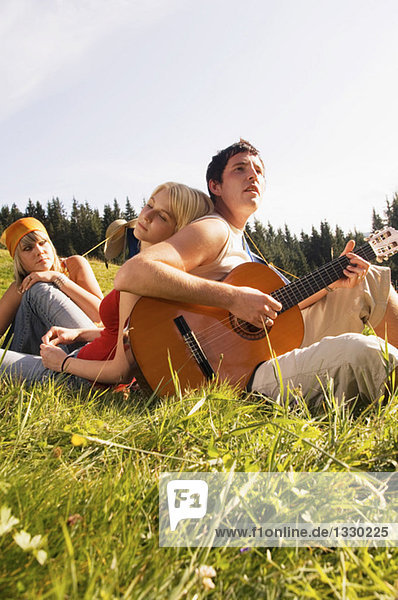 Young people in meadow  man playing guitar  low angle view