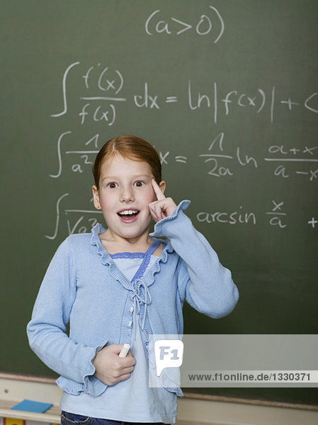 Girl (6-7) standing by blackboard,  solving arithmetic problem