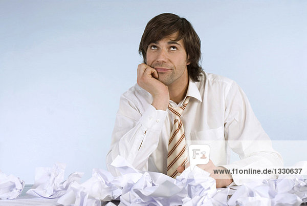 Man sitting at desk with crumpled papers  looking upwards