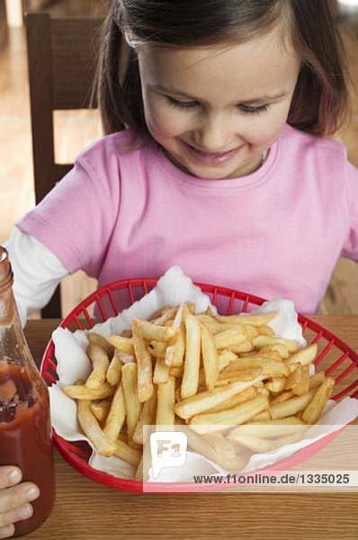 Small girl sitting in front of a basket of chips  ketchup