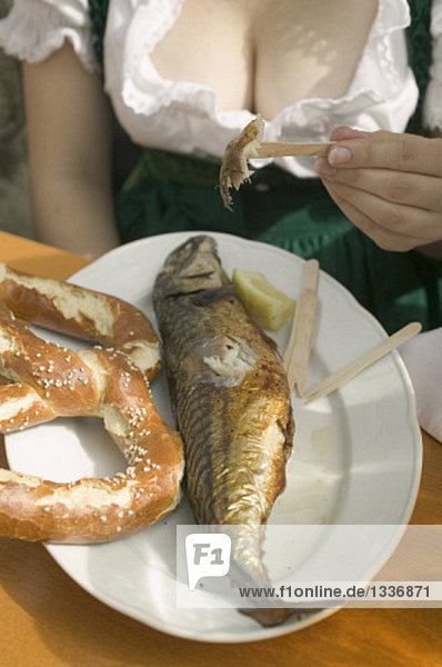 Frau isst Steckerlfisch mit Brezel beim Oktoberfest