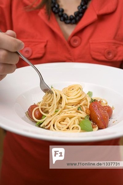 Frau isst Spaghetti mit Tomaten und Basilikum