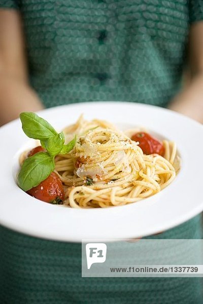 Frau hält Teller Spaghetti mit Parmesan und Basilikum
