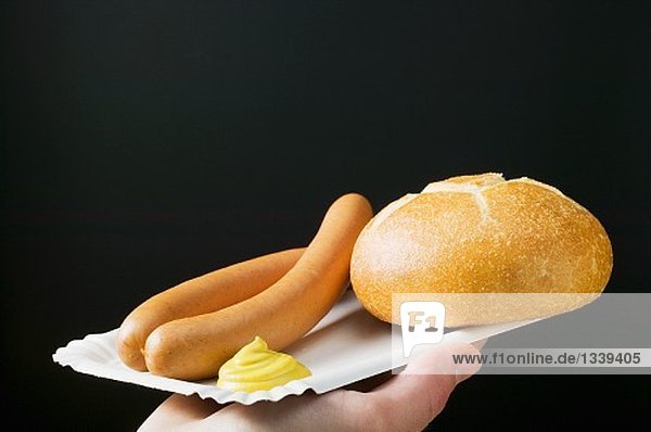 Hand hält Pappteller mit Wiener Würstchen, Brötchen und Senf