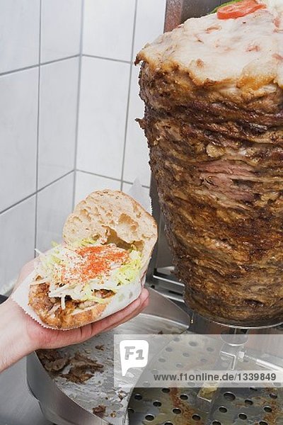 Hand hält Döner Kebab (aufgeklappt)  Fleisch am Drehspiess