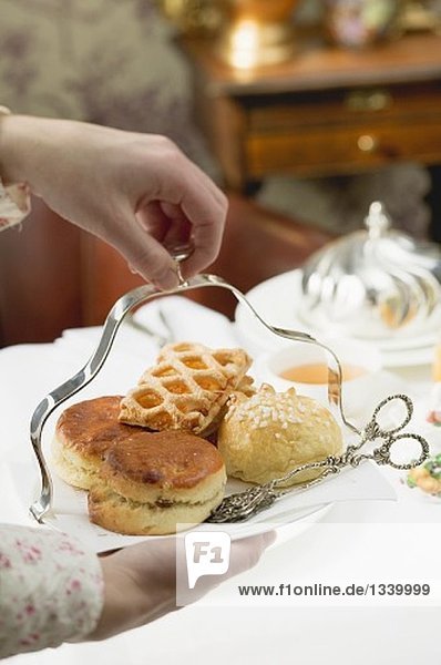 Hands serving sweet pastries and scones to eat with tea