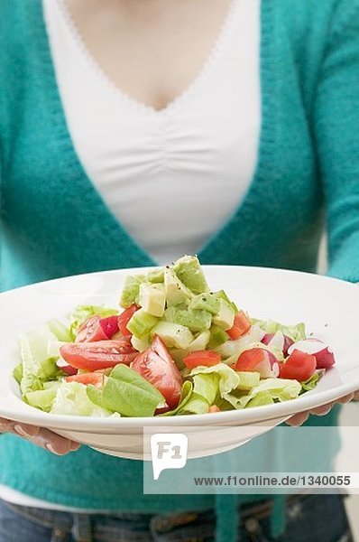 Woman holding plate of salad with avocados and tomatoes
