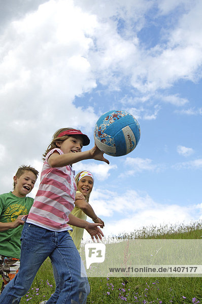 Drei Kinder spielen mit Ball im Feld