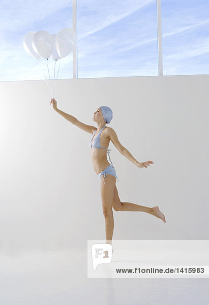 Young woman in bikini and swimming cap  holding white balloons