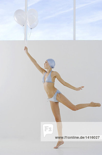 Young woman in bikini and swimming cap  holding white balloons