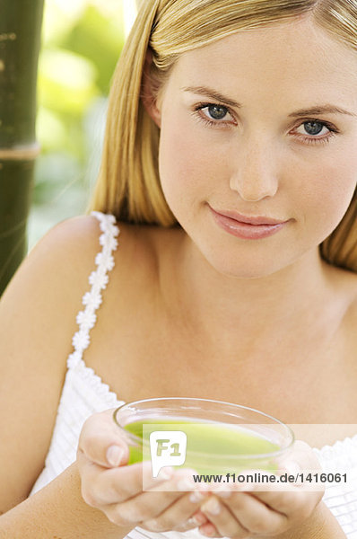 Porträt einer jungen Frau  die in die Kamera schaut  mit grüner Teetasse  im Freien.
