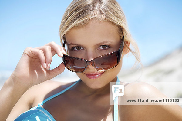 Porträt einer jungen Frau  die über ihre Sonnenbrille schaut