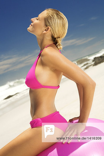 Junge Frau im rosa Bikini am Strand  sitzend auf einem großen Ball