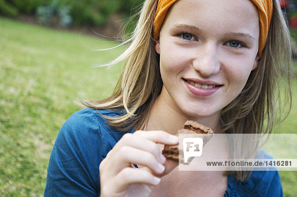Porträt eines Teenagermädchens  das ein Stück Kuchen hält  im Freien