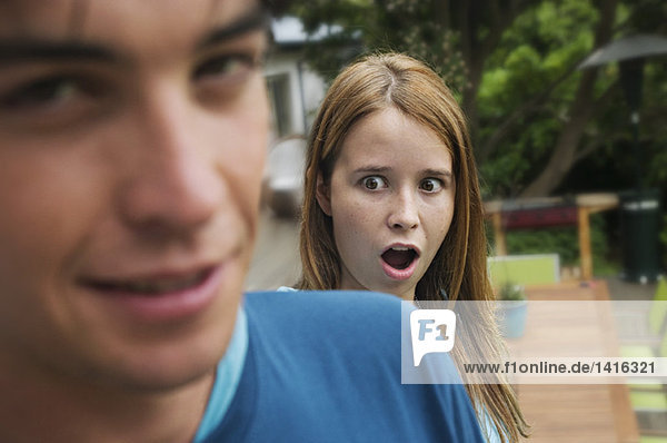 Surprised teenage girl with open mouth standing behind teenage boy