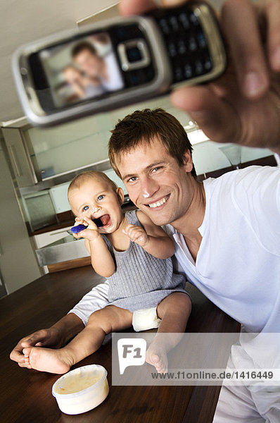Father and son in kitchen  man taking a photograph of themselves  indoors