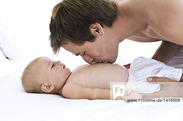 Portrait of a father kissing his baby's chest  lying on bed  indoors