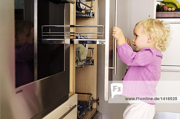 Little girl opening cabinets in kitchen  indoors