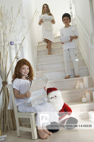 Drei Kinder  die Weihnachtsgeschenke anbieten  drinnen