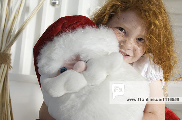 Weihnachtstag  Porträt eines kleinen Mädchens mit Kuscheltier (Weihnachtsmann)  drinnen