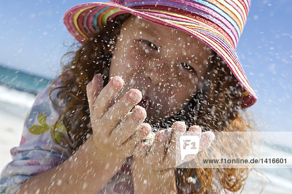 Porträt eines kleinen Mädchens  das Sand in die Hände bläst  im Freien