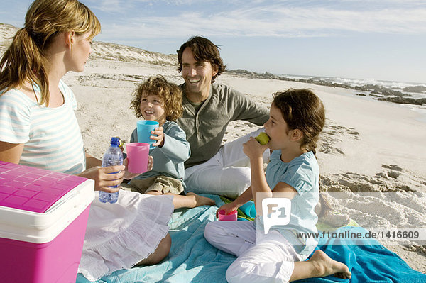 Eltern und zwei Kinder beim Picknick am Strand  im Freien