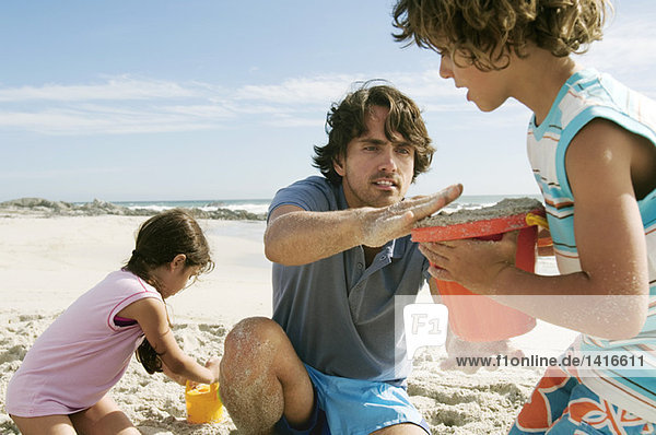 Vater und zwei Kinder beim Spielen am Strand  im Freien