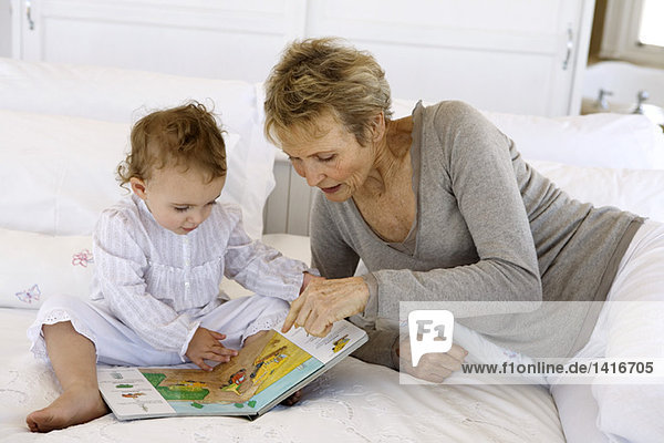 Seniorin beim Lesen mit kleinem Mädchen  auf dem Bett